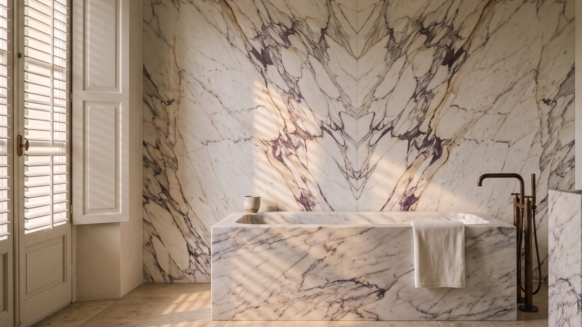 A book-matched Calacatta Viola marble bathroom, light falling through louvred shutters across the stone